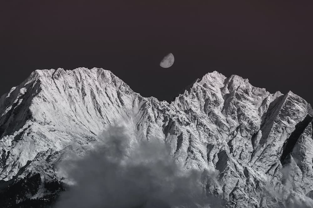 A snowy mountain range with the moon in the background